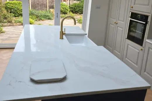 Calacatta Gold quartz island with subtle gold veining, white sink, curved brass mixer tap and glazed garden doors